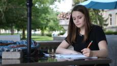 学生坐在外面的桌子旁，在纸上做笔记.